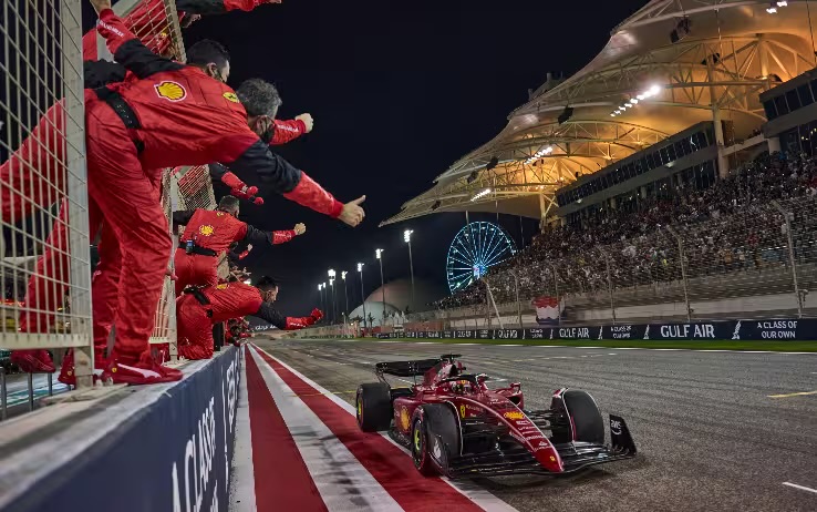 Ferrari vincente al Gran Premio del Bahrain, con il team che festeggia a bordo pista sotto le luci notturne.