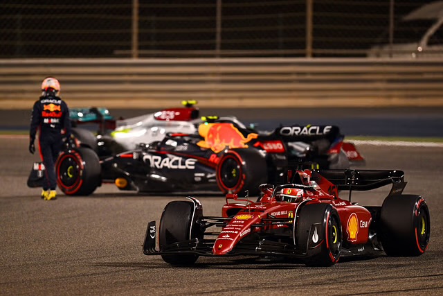 Una Ferrari rossa in primo piano con un'illuminazione notturna in pista, mentre sullo sfondo si intravedono altre vetture da corsa, inclusa una Red Bull e una Mercedes in Bahrain 