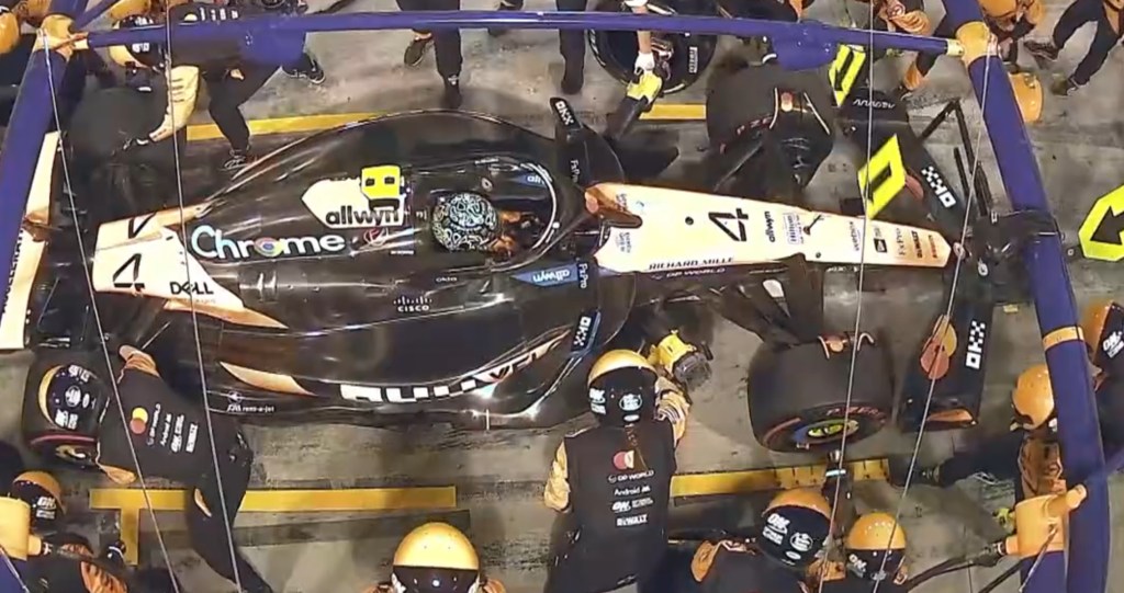 Una McLaren nel box, con il pilota Lando Norris seduto all'interno mentre la sua squadra esegue un pit stop con vari meccanici attivi attorno all'auto.