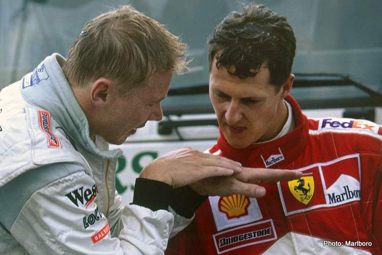 Mika Hakkinen e Michael Schumacher si confrontano nel parco chiuso dopo una gara di Formula 1, discutendo animatamente. Hakkinen vs Schumacher.